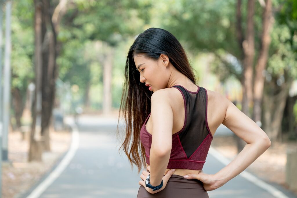 Back of Asian sport woman show action of waist or back pain after exercise in park