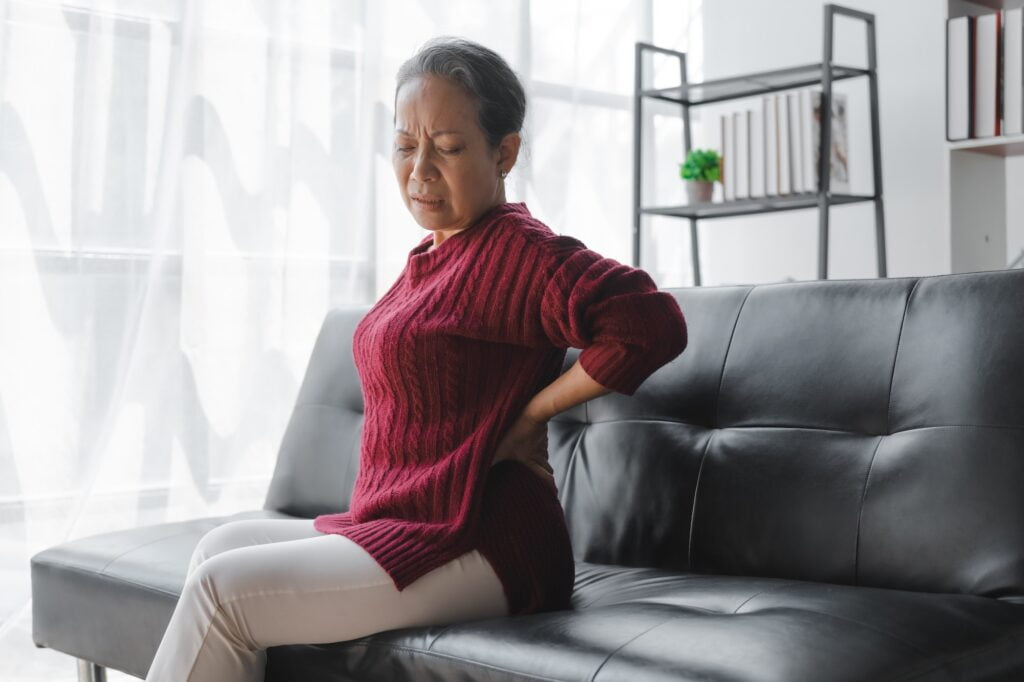 Elderly asian housewife woman sitting on sofa. Back pain, lumbar pain, cervical spine