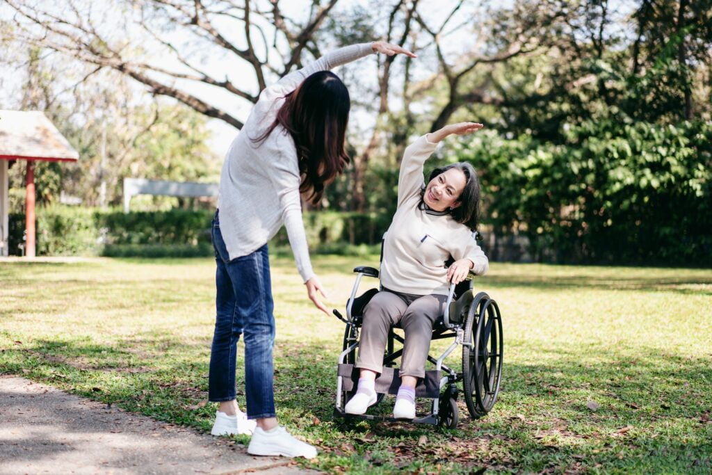 Young asian woman exercise with mother on wheelchair in the garden while senior woman and daughter