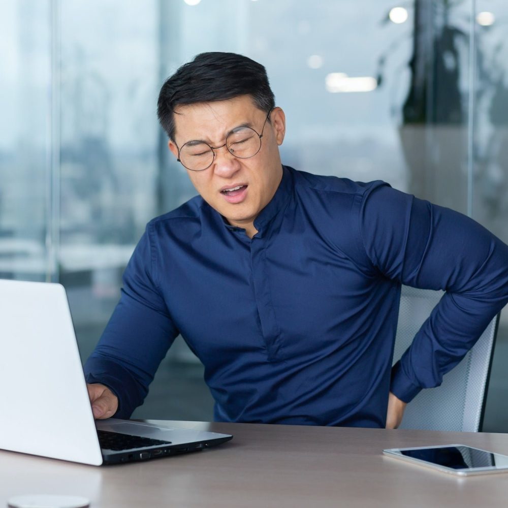 Sick overworked man at work, businessman has severe back pain, asian man holding hand on side
