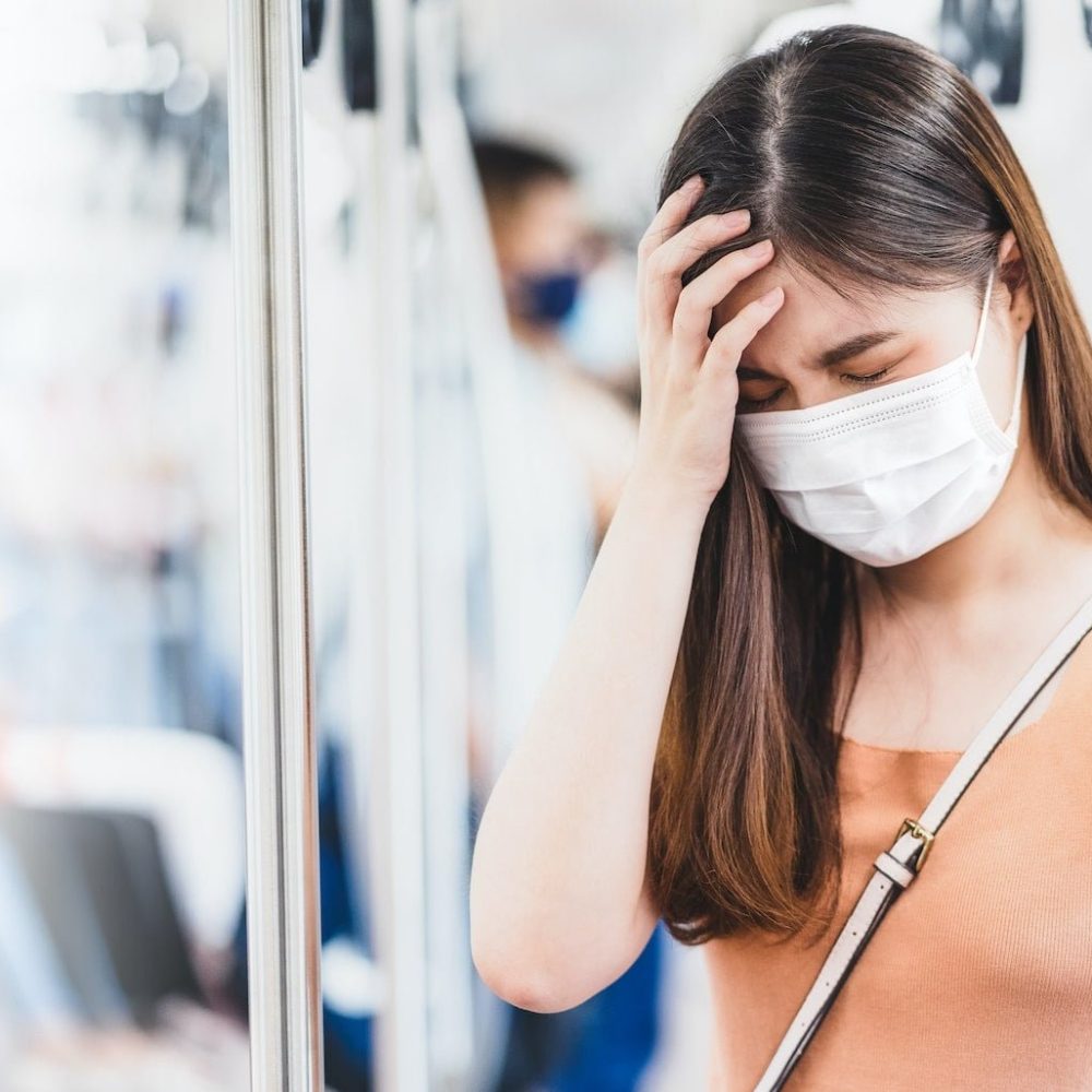 Young Asian woman passenger wearing surgical mask and Having a headache in subway train